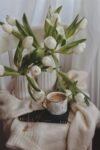 elegant composition of tulips bunches and cup of hot drink placed on knitted sweater