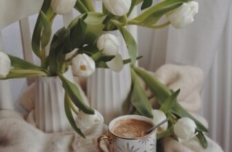 elegant composition of tulips bunches and cup of hot drink placed on knitted sweater